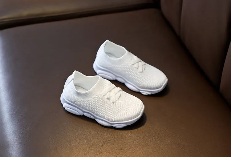 Children's white fabric lazy slip-on shoe with non-slip rubber sole on a wooden floor.