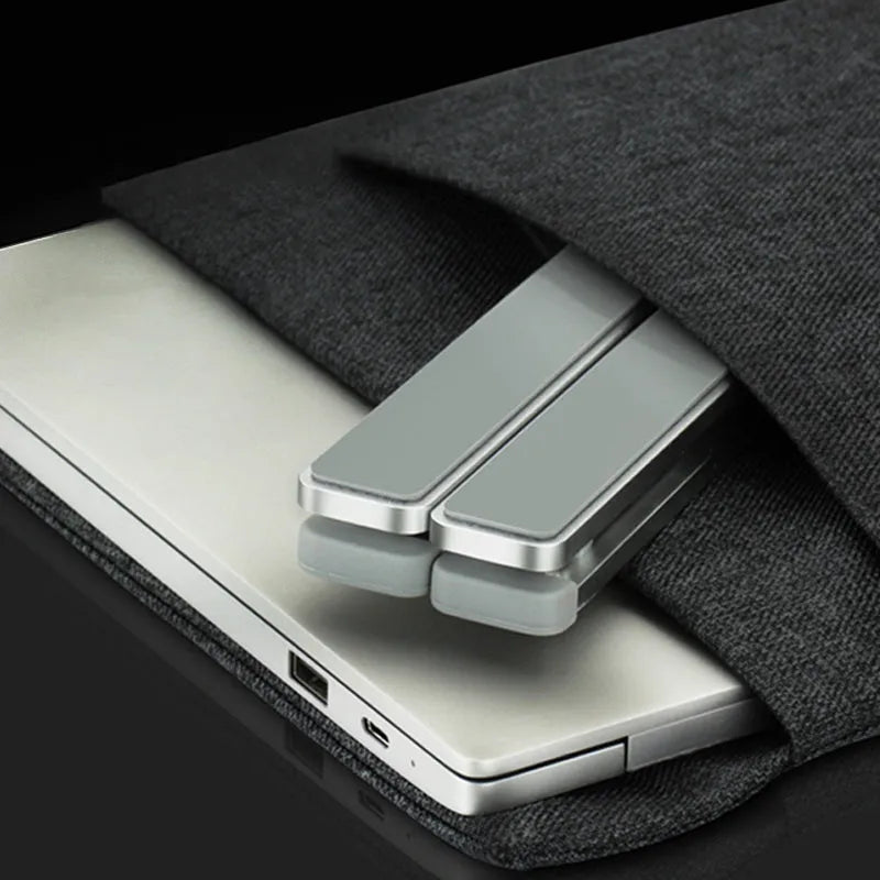 Folding laptop stand in silver with adjustable angle, holding a laptop, showing hollow bottom and non-slip silicone pads