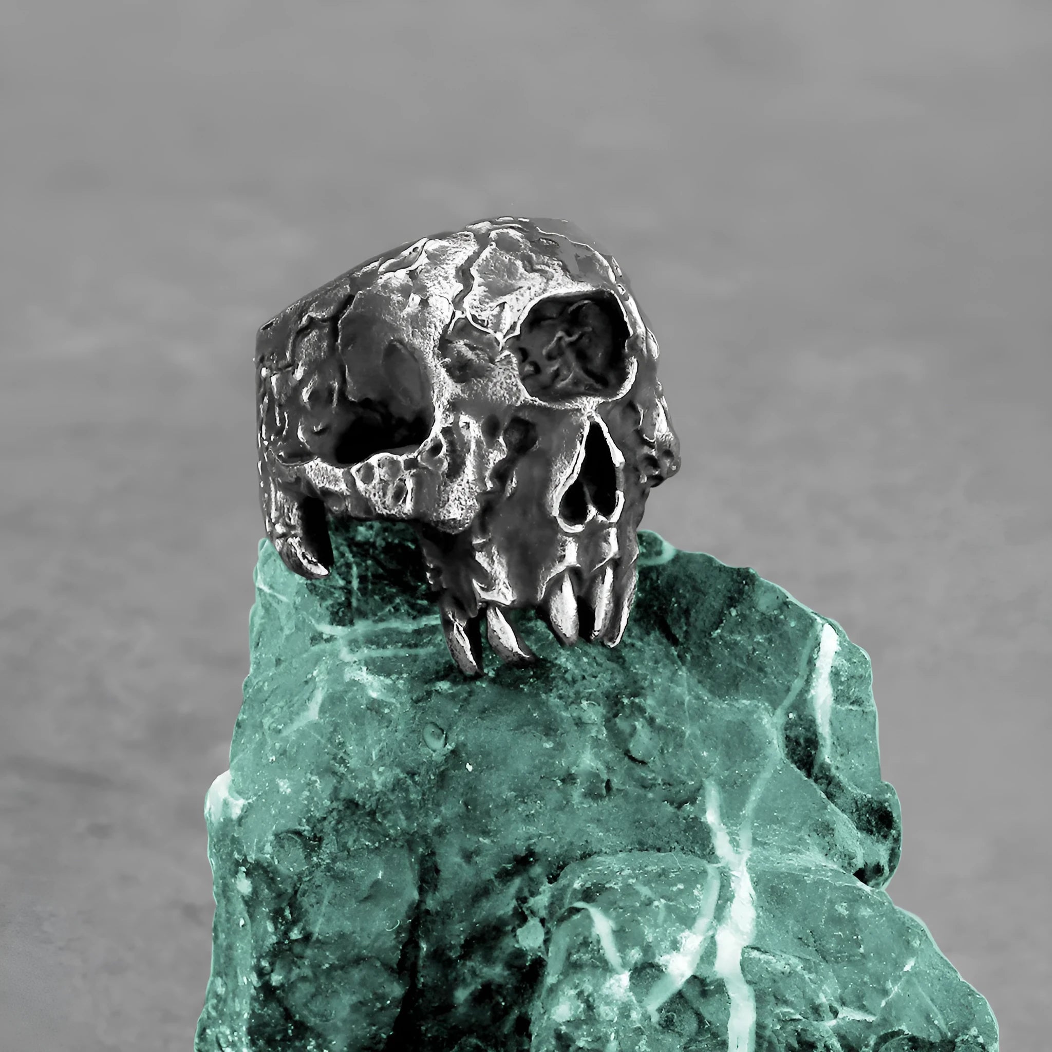 A silver-toned alloy ring featuring a detailed one-eyed skull design on a black background.