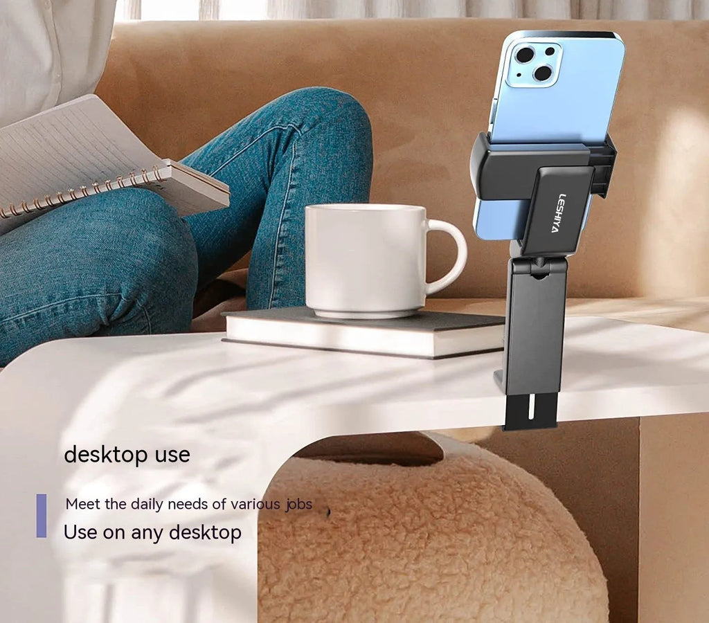 A black foldable rotating lazy phone holder gripping a mobile smartphone on a desk.