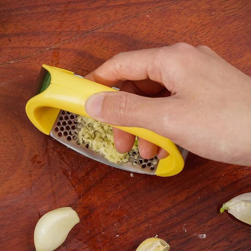 Stainless steel garlic press with ergonomic handle in assorted colours on a kitchen counter.