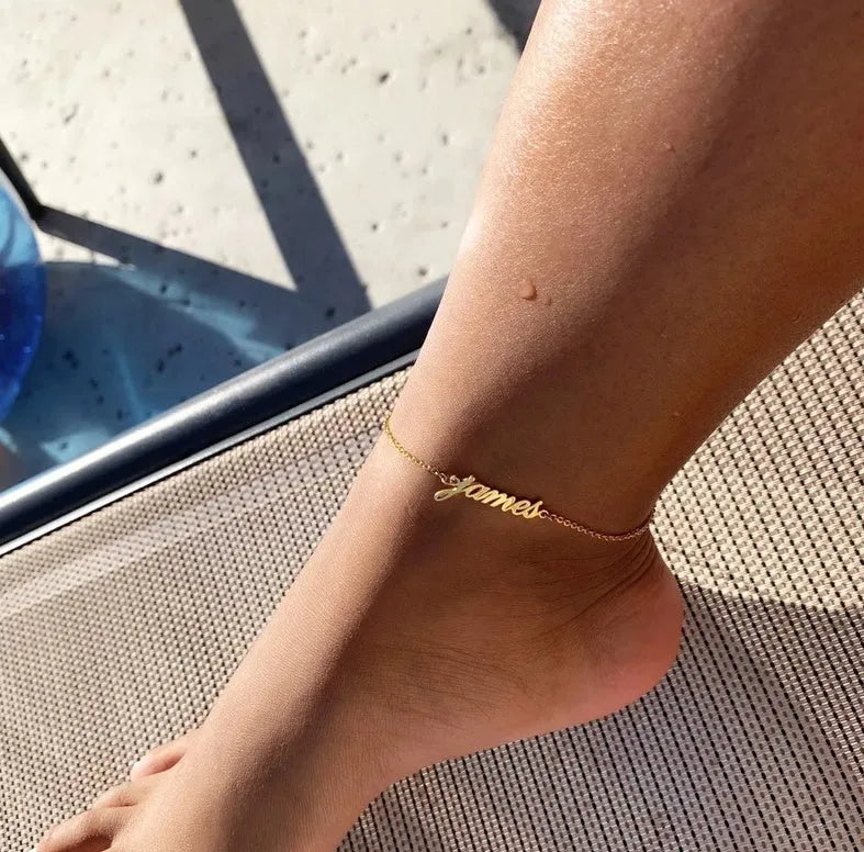 Gold titanium steel cable chain anklet with personalised name engraving on a sandy beach background