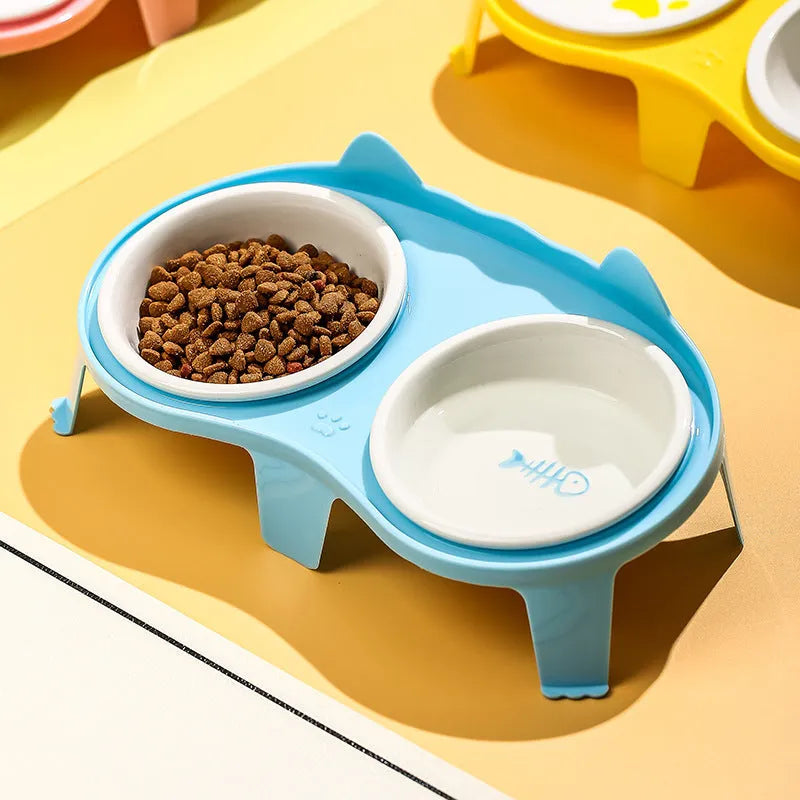 Blue ceramic cat food and water bowl set on a white stand with a hook, showing tilted feeding angle.