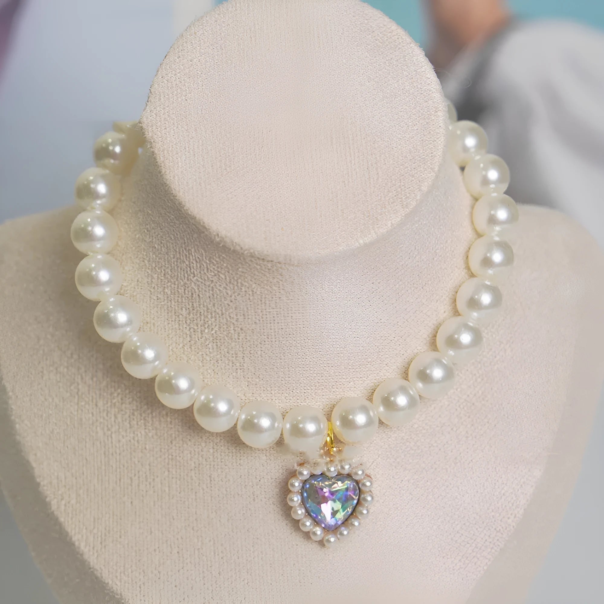 Pearl necklace cat collar with heart-shaped gem charm in various colours on a white background.