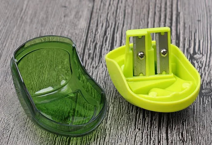 A double hole manual pencil sharpener in a random colour on a white background.