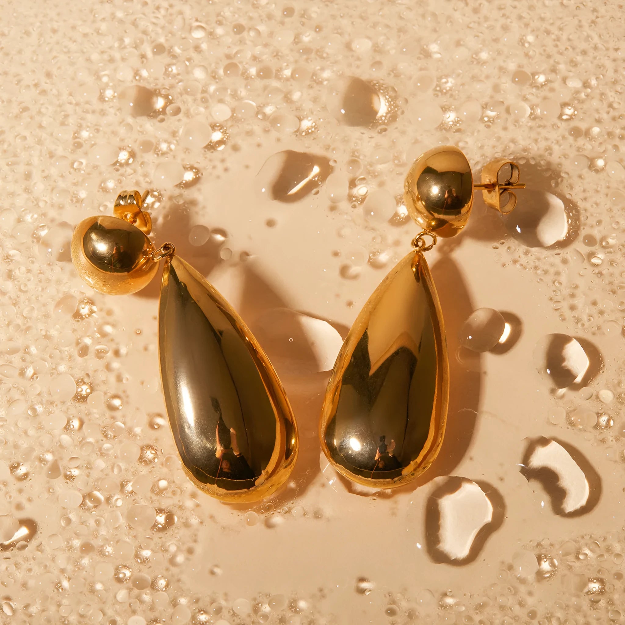 Gold-colour stainless steel pendant earrings with geometric hemisphere and water drop design.