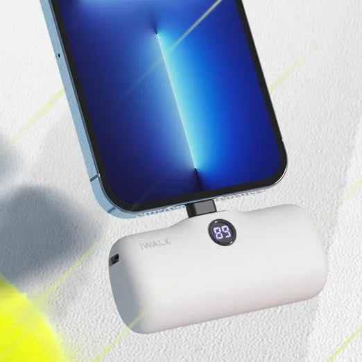 Small white cylindrical lipstick-style power bank showing digital battery percentage screen on a wooden table.