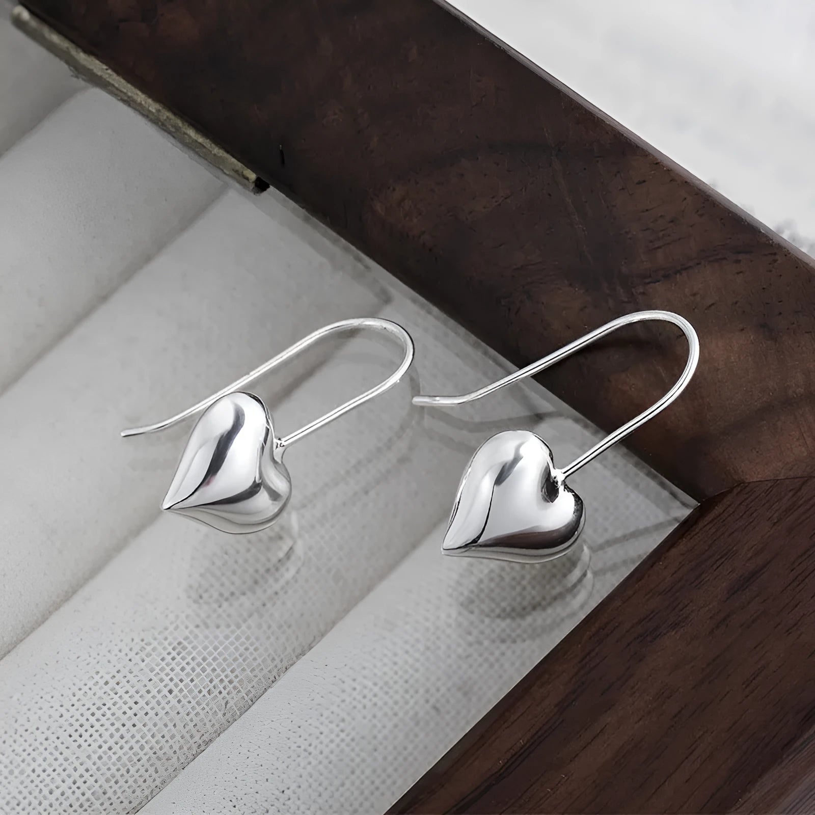 Silver glossy 3D heart-shaped earrings with Korean style hooks on a white background.