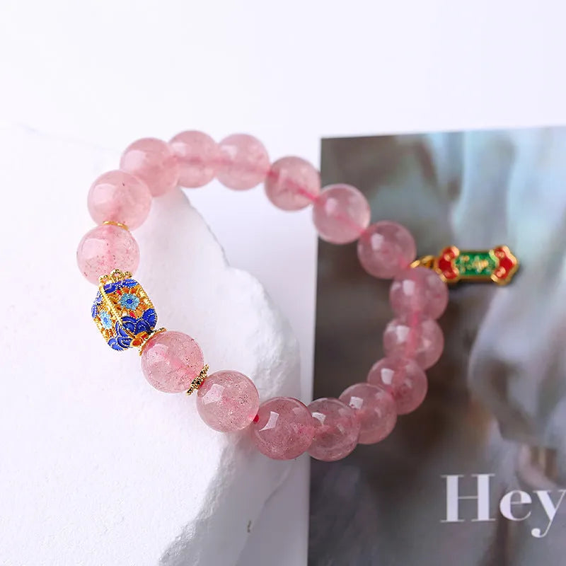 Close-up of a pink strawberry quartz crystal bracelet with hand-woven Ruyi design and letter detailing.