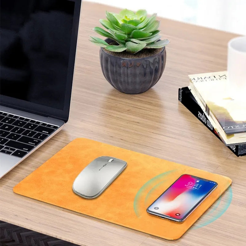Brown leather wireless charging mouse pad on a wooden desk with a phone charging on it.