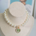 Pearl necklace cat collar with heart-shaped gem charm in various colours on a white background.