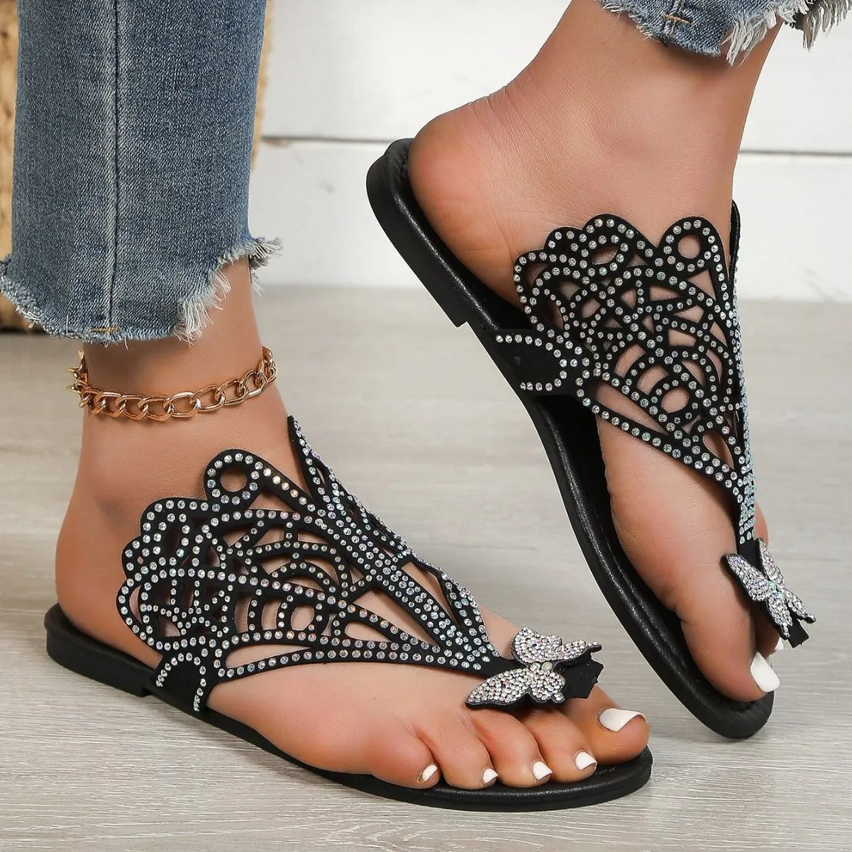 Women's black slip-on sandals with rhinestone details, a flip-toe strap, and a flat rubber sole.