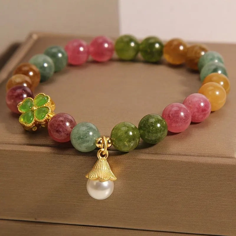 Natural colour tourmaline bracelet with four-leaf clover pearl pendant, geometric drop shape on woman's wrist.