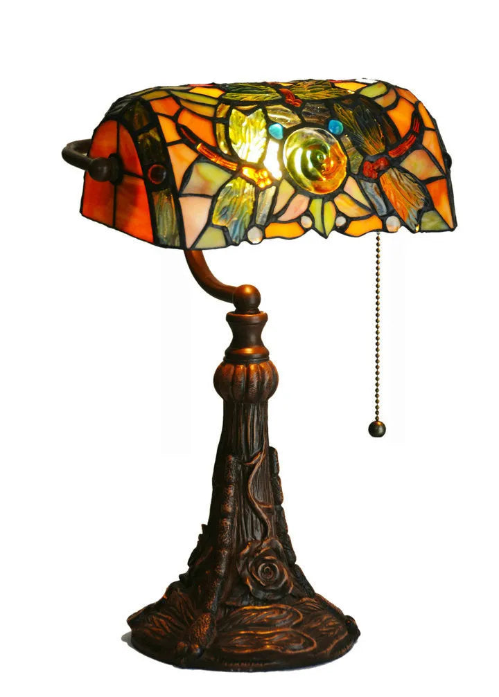 Tiffany style table lamp with coloured stained glass shade and resin base on a desk.