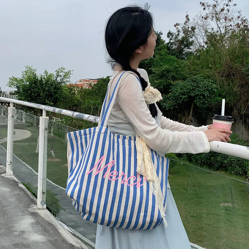Blue striped letters printed on a pink, blue and white striped cotton canvas bag.