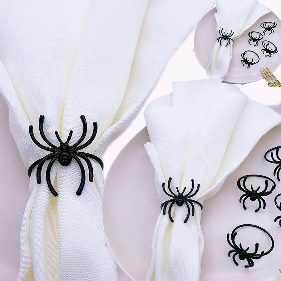 Six black alloy spider-shaped napkin rings for Halloween table decoration on a dark tablecloth.