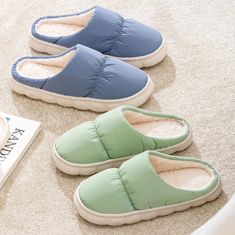 A pair of blue down cotton winter slippers with a thick rubber sole and plush lining on a wooden floor.