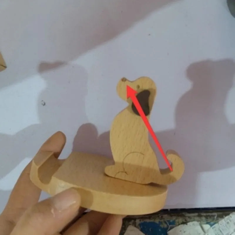 Solid beech wood mobile phone stand with a resin cow figurine and a slot for holding coins on a wooden desk.