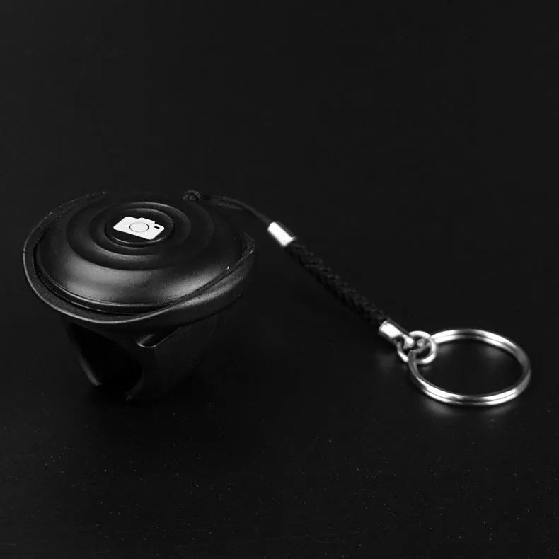 Small black Snap Bluetooth remote control for smartphone and camera shutter release, shown on a hand for scale.