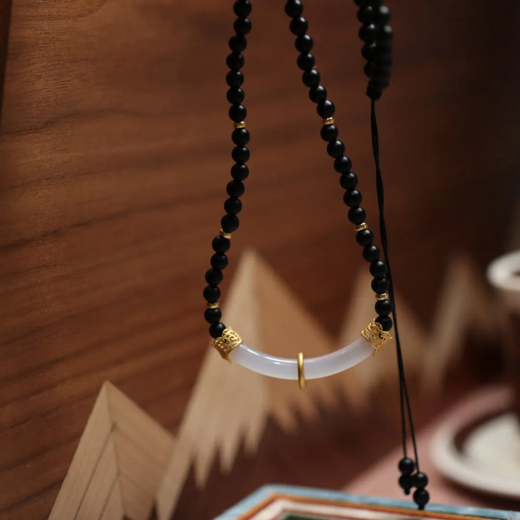 Close-up of a Chinese style U-shaped necklace with a frosted black agate and white chalcedony pendant on a silver ball bead chain.