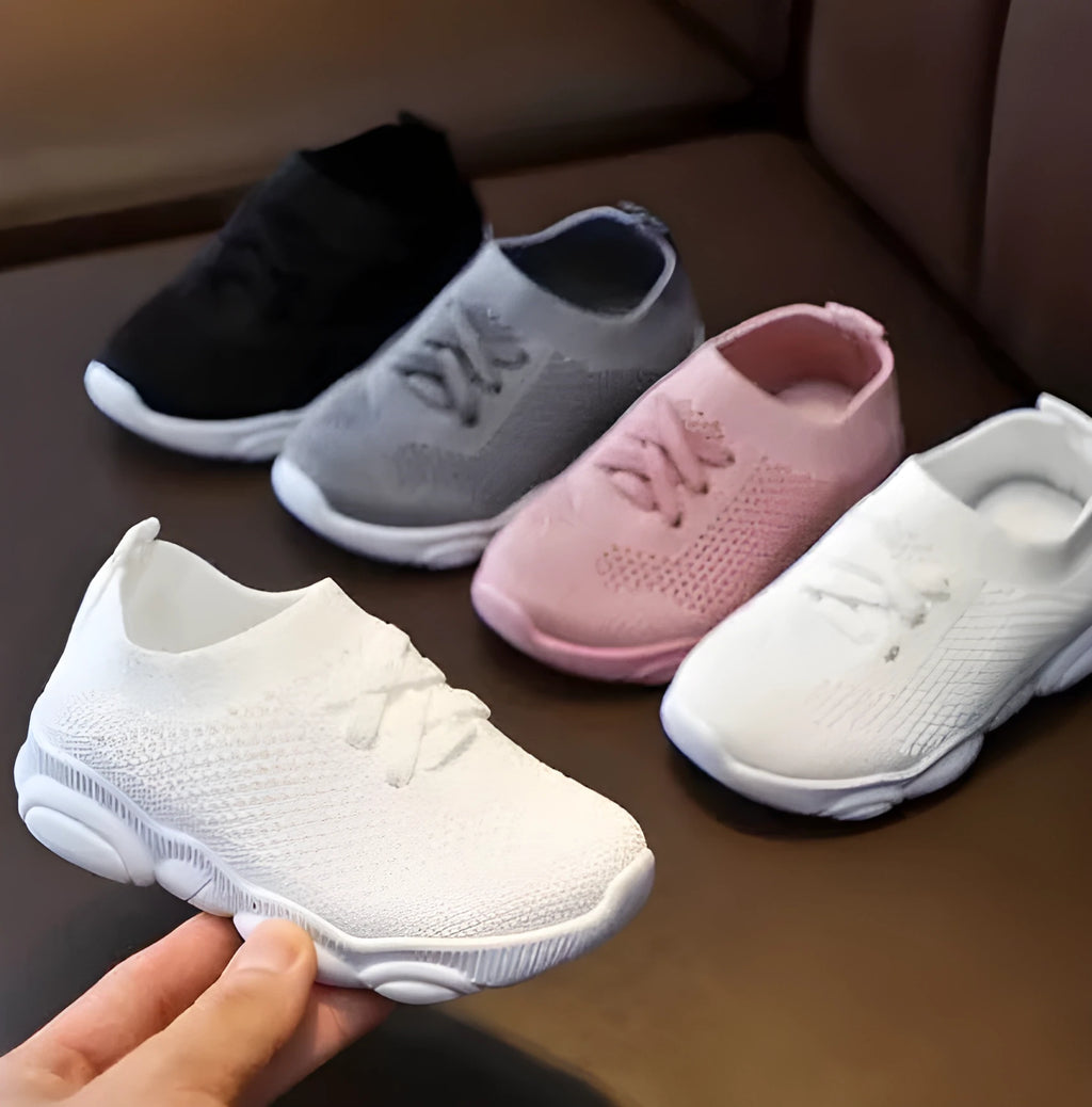Children's white fabric lazy slip-on shoe with non-slip rubber sole on a wooden floor.