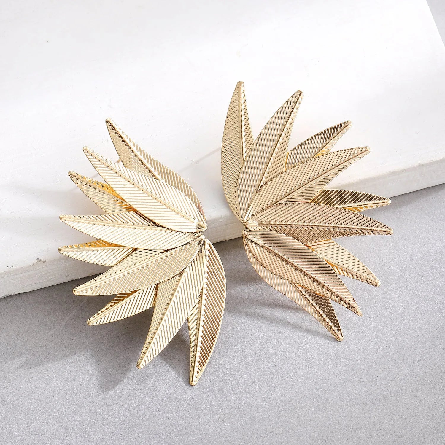 Gold and white alloy leaf shape patch earrings on a flat surface
