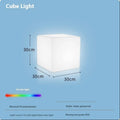 A white square cube LED stool light sitting on a patio, illustrating its modern design and outdoor use.