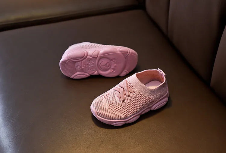 Children's white fabric lazy slip-on shoe with non-slip rubber sole on a wooden floor.