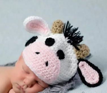 Hand-knitted white baby cow suit set with matching hat and pants on a newborn