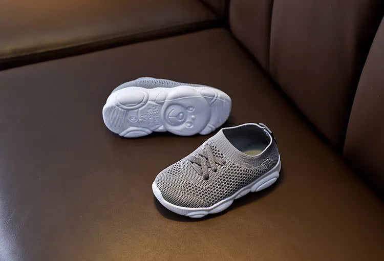 Children's white fabric lazy slip-on shoe with non-slip rubber sole on a wooden floor.