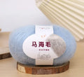Single 100g ball of mohair yarn in a chosen colour next to a hand-woven light grey scarf sample.