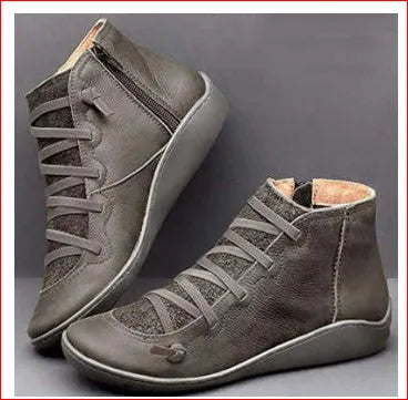 Women's black flat casual ankle boot with round toe and low wedge heel on a wooden floor.