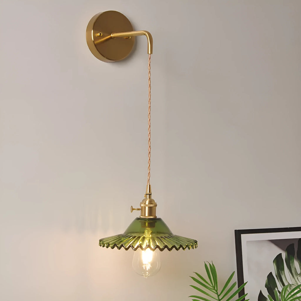 Retro brass lotus wall lamp with a 22cm green glass shade mounted on a copper base beside a bed.