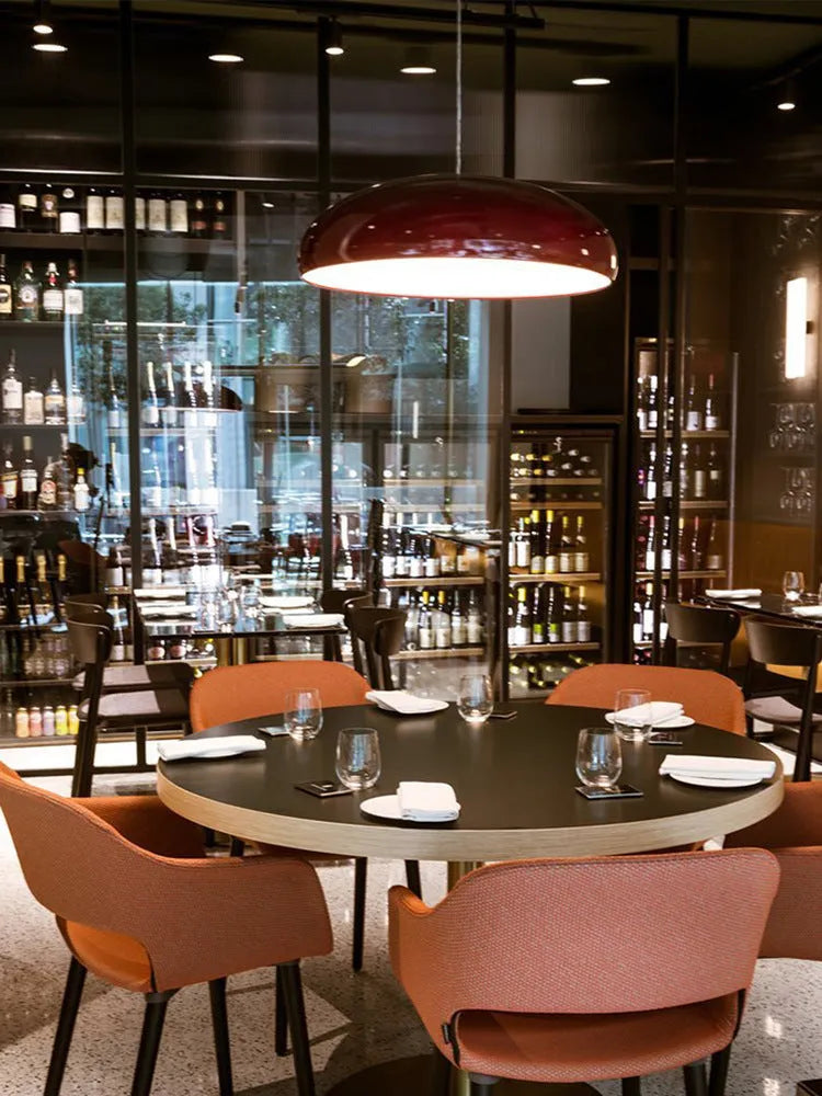 Orange iron Danish-style pendant lamp with adjustable cable above a restaurant table.