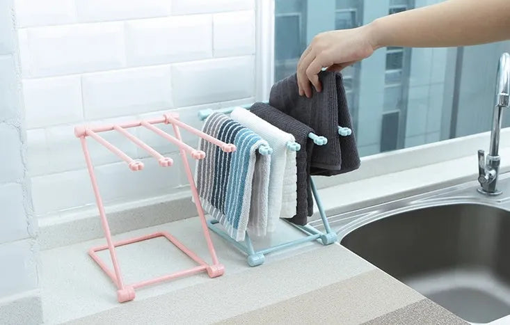 Light grey foldable plastic dishcloth shelf mounted on a wall holding towels.