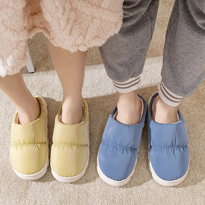 A pair of blue down cotton winter slippers with a thick rubber sole and plush lining on a wooden floor.