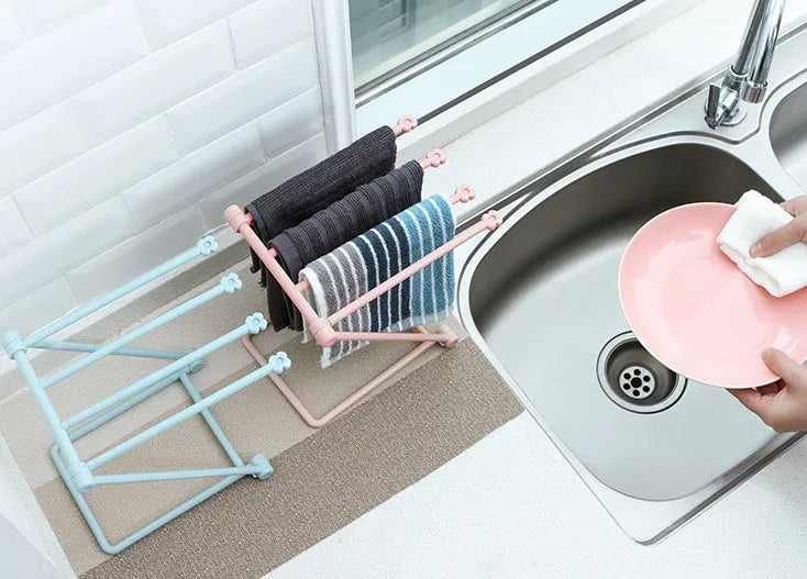 Light grey foldable plastic dishcloth shelf mounted on a wall holding towels.