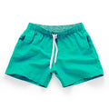 Men's straight-leg polyester surf shorts on a beach, showing colour options like black, fluorescent yellow, and navy blue.