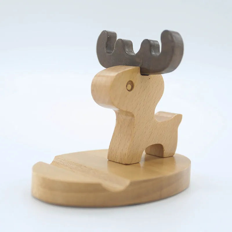 Solid beech wood mobile phone stand with a resin cow figurine and a slot for holding coins on a wooden desk.