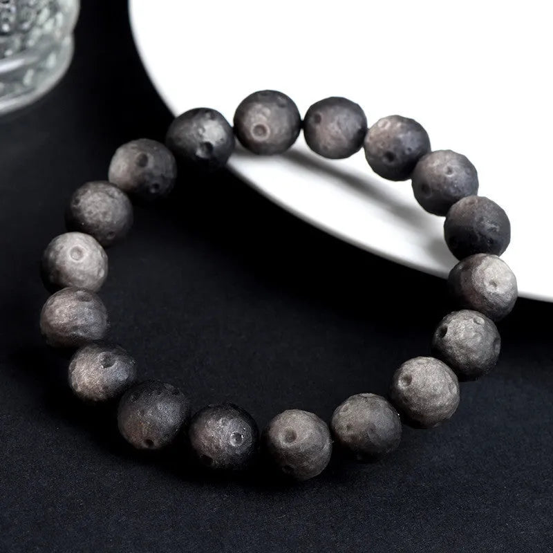 Obsidian crater ball bracelet on a wrist, showing ground stone texture and bead size.
