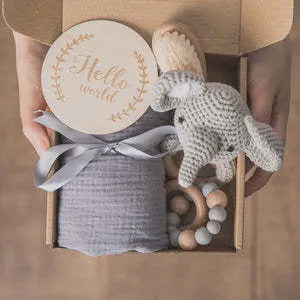 Baby teething toy gift set showing gauze blanket, wooden bell, gum teether, tire brush, and milestone on white background