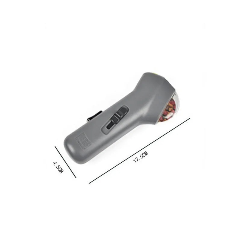 Grey pet snack catapult launcher toy on grass, showing spring trigger and treat slot.