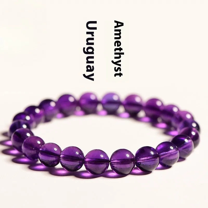 Natural violet amethyst crystal bead bracelet with polished, scattered beads on a neutral background.