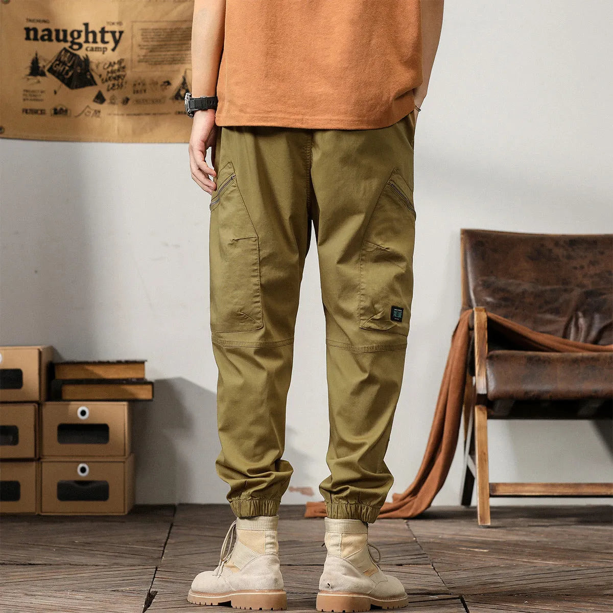Man wearing khaki coloured cotton overalls with tapered legs and elasticated ankle bands.
