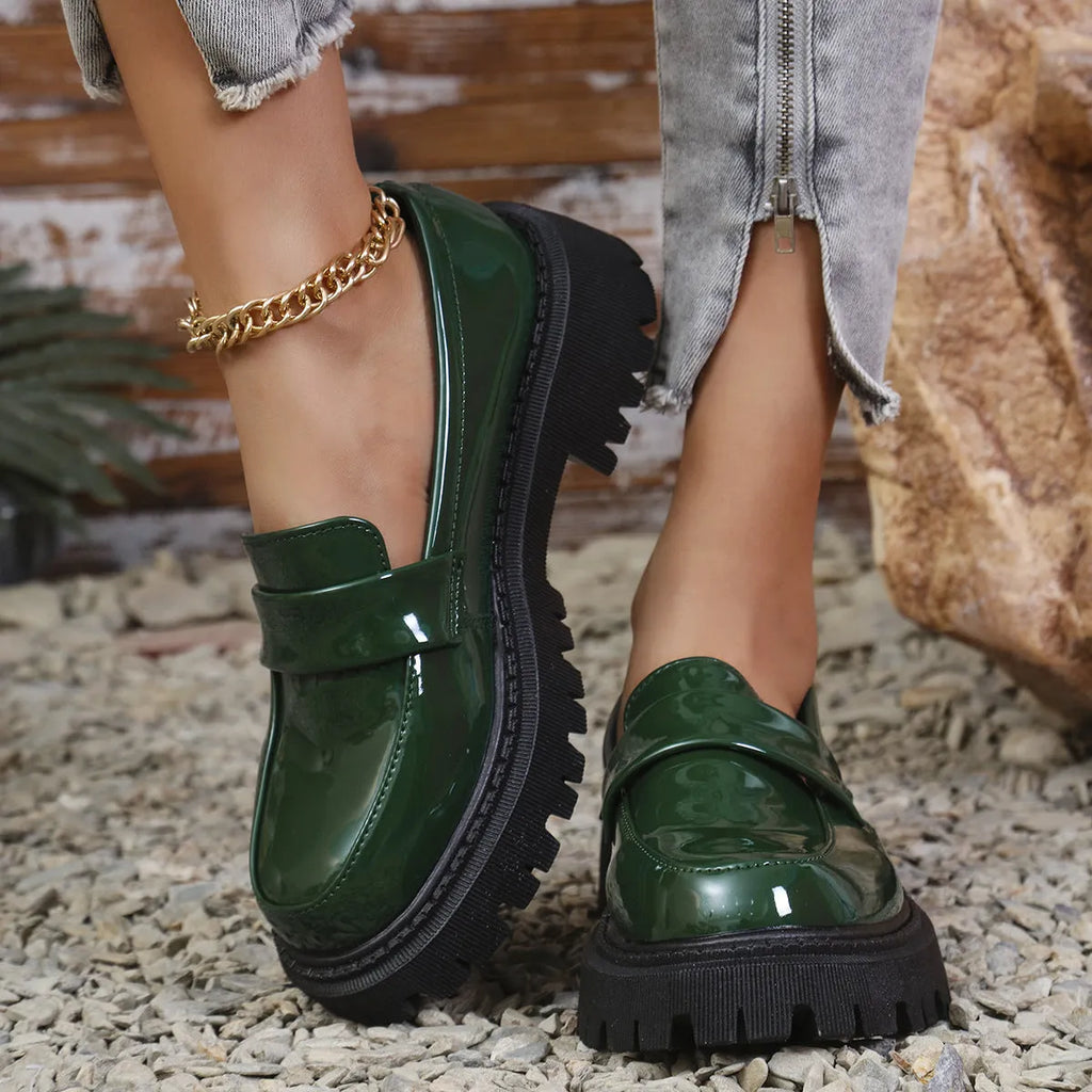 Black British style slip-on loafers with a chunky platform heel and thick rubber sole on a plain background.
