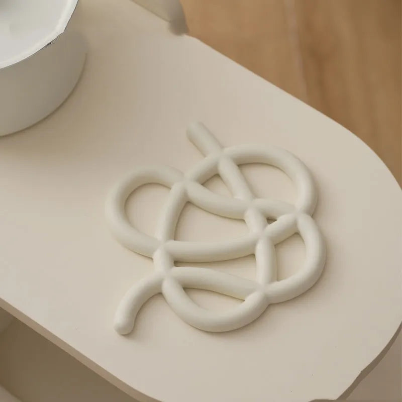 Modern irregular-shaped ceramic heat proof mat in grey protecting a wooden dining table from a hot pan.