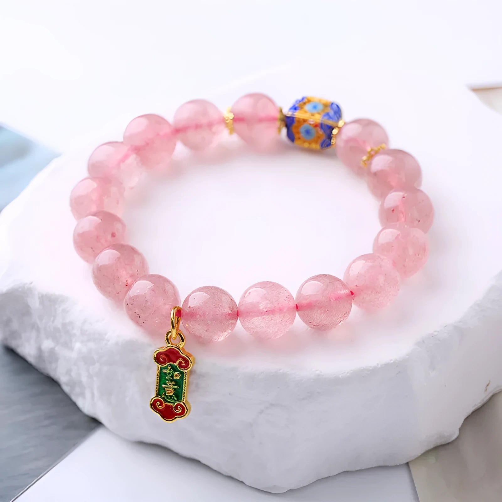 Close-up of a pink strawberry quartz crystal bracelet with hand-woven Ruyi design and letter detailing.