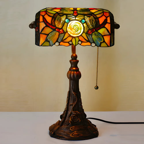 Tiffany style table lamp with coloured stained glass shade and resin base on a desk.