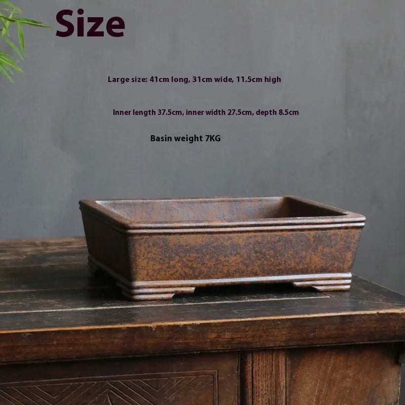 Rectangular purple sand bonsai pot with burnt pine tree decoration, shown on a garden surface.