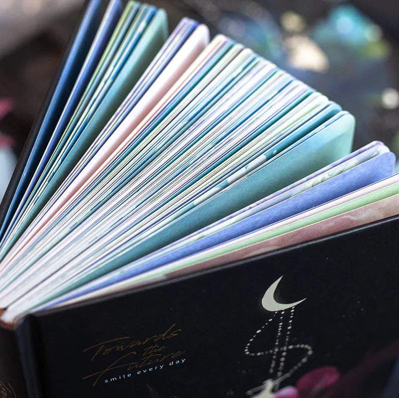 A5 notebook with a luminous cover shown in deep blue, open to reveal pages with colour illustrations.
